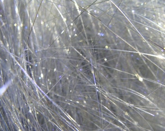 May include: Close-up of a shimmering, textured surface with fine, silver strands and scattered, sparkling highlights. The strands appear to be interwoven, creating a soft, luminous effect. The overall appearance is delicate and ethereal.