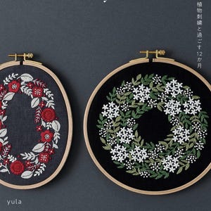 May include: Two circular wooden embroidery hoops containing fabric with floral designs. The left hoop features red flowers and white leaves on dark fabric. The right hoop displays white flowers and green leaves on black fabric. Text reads yula and KADOKAWA.