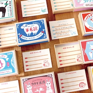 Peut inclure: Une collection de boîtes de papeterie rectangulaires style boîte d'allumettes avec des illustrations colorées d'animaux comme des chats, un mouton, un panda, un pingouin et un lapin, du texte japonais et des cartes internes avec des allumettes.