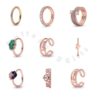 Op de afbeelding: Negen roségouden ringen worden getoond, met verschillende ontwerpen. Deze omvatten ringen met heldere stenen, smaragdgroene stenen en een kroonontwerp. Sommige ringen hebben een band van kleine stenen, terwijl andere unieke vormen en versieringen hebben.