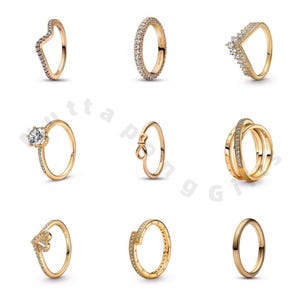 Op de afbeelding: Negen goudkleurige ringen met verschillende ontwerpen worden getoond. Stijlen zijn onder meer een chevronvorm, een band volledig bezet met kleine steentjes, een ring met een grote centrale steen en een ring met een strikdesign. De ringen staan tegen een witte achtergrond.