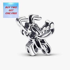 Pode incluir: Um charm de prata com um design estilizado. O charm tem uma aparência tridimensional com linhas curvas e um acabamento polido. O texto "BUY TWO GET ONE FREE" está em uma caixa azul e vermelha no canto superior esquerdo.