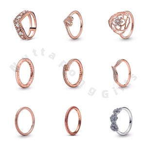 Può includere: Una collezione di anelli in oro rosa con vari design. Alcuni anelli presentano pietre preziose trasparenti, mentre altri hanno forme uniche come una V o un motivo floreale. Un anello è in argento con tre gruppi di pietre preziose trasparenti.
