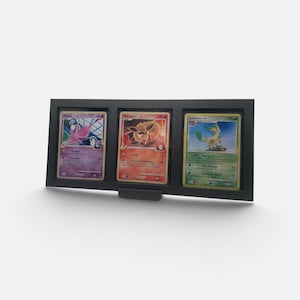 May include: A black display frame holding three Pokémon trading cards. The cards feature various Pokémon characters with colourful designs. The frame has a simple, modern design, suitable for showcasing collectible cards.