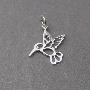 May include: Silver hummingbird charm with a delicate cutout design. The charm has a loop at the top for attaching to a necklace or bracelet.