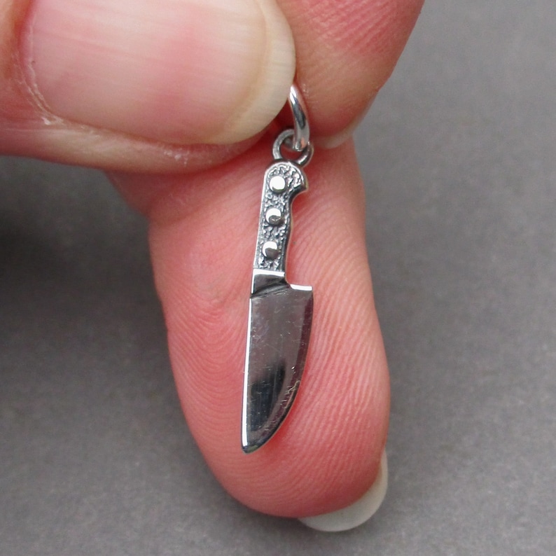 May include: Silver charm in the shape of a chef's knife. The knife has a detailed handle and a sharp blade.