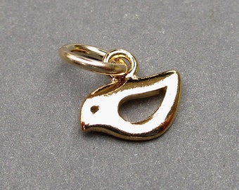 May include: A small, gold-toned metal charm shaped like a stylized bird in flight. The charm features a smooth, reflective surface with a cutout center and a circular jump ring attached to the top for hanging. The bird is depicted in profile.