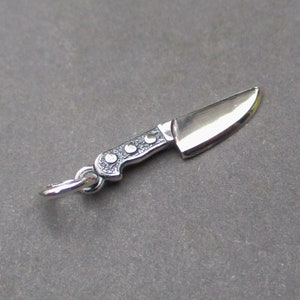 May include: A silver knife charm with a detailed handle and a sharp blade. The charm has a loop for attaching to a necklace or bracelet.