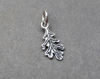 May include: A small, silver-colored metal charm shaped like an oak leaf with detailed, raised veins and scalloped edges. The charm features a circular jump ring attached to the top stem, allowing it to be suspended from a chain or bracelet.