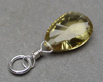 May include: A faceted, pear-shaped, translucent yellow-brown gemstone pendant. The stone is secured by a silver-coloured metal wire wrap that connects to a circular silver-coloured metal jump ring at the top, creating a simple jewellery component.