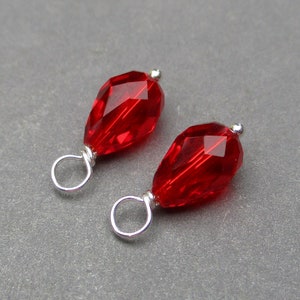 May include: Two red crystal teardrop shaped beads with silver jump rings. The beads are faceted and have a shiny finish.