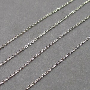 May include: Four parallel silver-toned metal chains arranged diagonally across the frame. Each chain consists of a series of small, uniform, interlocking circular links that create a continuous, delicate, and reflective metallic strand structure.