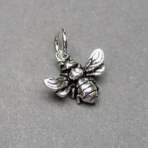 May include: Silver charm in the shape of a bee with detailed wings and a textured body.