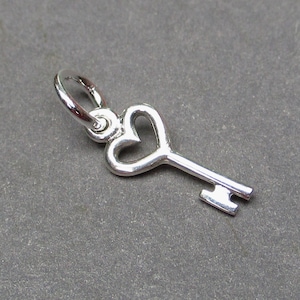 Puede incluir: Colgante de llave plateada con diseño de corazón. La llave tiene un lazo para sujetarla a una cadena o pulsera. El mango de la llave tiene forma de corazón y los dientes son rectangulares.