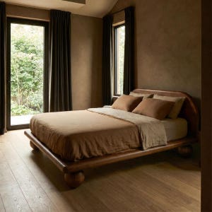 May include: A low-profile wooden bed frame featuring a rounded headboard and four spherical ball-shaped feet. The bed is dressed in a tan linen duvet cover and two matching tan pillows, positioned within a room with dark brown walls and curtains.