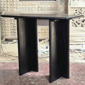 May include: A small, black wooden table with a rectangular top and two wide, vertical supports. The table is approximately 30 inches long and 15 inches wide, with a height of about 28 inches. The design is minimalist and modern.