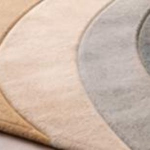 May include: A close-up of four crescent-shaped rugs in varying shades of beige, cream, gray, and blue. The rugs have a soft, textured appearance, with a subtle border outlining each shape. The arrangement suggests a layered or decorative display.