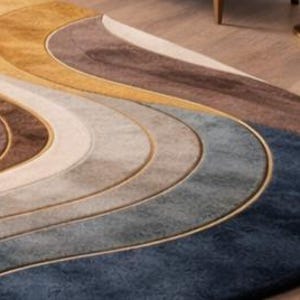 May include: A modern, abstract area rug with a wave-like design. The rug features a gradient of colors, including shades of blue, gray, brown, and gold. The rug is made of a soft material and has a gold border. The rug is a decorative home decor item.