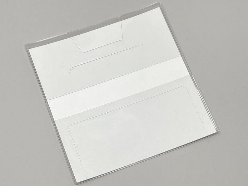 May include: Clear plastic checkbook cover with a white interior. The cover has a rectangular shape with a transparent design, featuring a pocket and a flap for securing checks. The checkbook cover is designed to protect and organize checks.