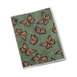 May include: A green notebook with a clear plastic cover. The cover features a repeating pattern of orange butterflies.