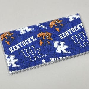 May include: A blue and white checkbook cover with the University of Kentucky Wildcats logo and the words "Kentucky" and "Wildcats".
