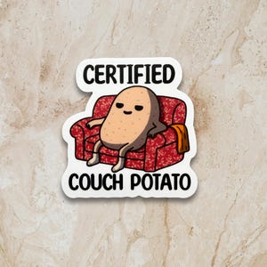 May include: A sticker depicting a cartoon potato relaxing on a red patterned sofa. The potato has a relaxed expression. The text "CERTIFIED COUCH POTATO" is above and below the image in white block letters.