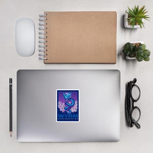 May include: A sticker featuring a stylized dragon design in shades of blue and purple, set against a striped background. The text "WYRM ENGINEERING" is displayed below the dragon. The sticker is rectangular and likely made of vinyl.