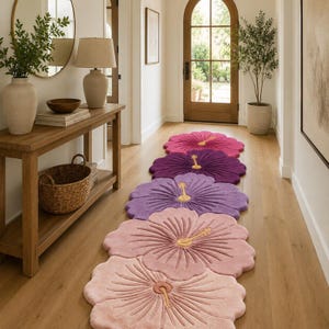 May include: A long runner rug featuring a series of five connected flower-shaped segments in a gradient of colors, ranging from deep magenta and purple to light lavender, soft pink, and pale peach, each with a central yellow stamen detail.