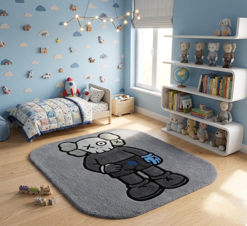 K&ouml;nnte beinhalten: Ein grauer rechteckiger Teppich mit einer Cartoonfigur in einem schwarzen Anzug, wei&szlig;em Kopf und durchgestrichenen Augen. Der Teppich befindet sich in einem Kinderzimmer mit Bett, Regalen mit Spielzeug und einer blauen Wand mit Wolken- und Raketendekorationen.