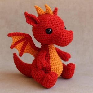 Pode incluir: Um dragão de crochê feito à mão em vermelho e laranja. O dragão tem olhos grandes e pretos, asas laranja e detalhes laranja na cabeça e na barriga. O dragão está sentado com as pernas cruzadas e os braços ao lado. Um brinquedo fofo e divertido.