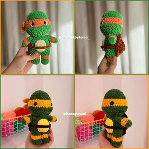 May include: A plush crochet turtle doll featuring a green body, an orange eye mask, and a brown shell. The doll has a round head, black eyes, and a light-colored circular patch on its belly. The texture is soft and fuzzy, with visible yarn stitches.