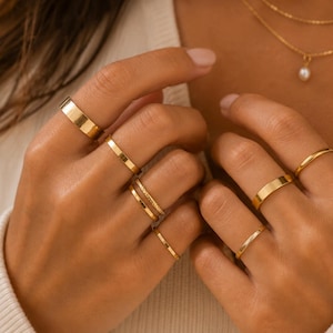 May include: Several gold rings of different designs are displayed on fingers, including a flat band, a slim band, and rings with textured patterns. A fine gold necklace with a pearl pendant is also shown.