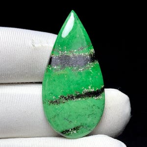 May include: A teardrop-shaped gemstone with a vibrant green hue, accented by bands of black and silver. The polished surface reflects light, highlighting the natural patterns within the stone. This gemstone is likely for jewelry making.