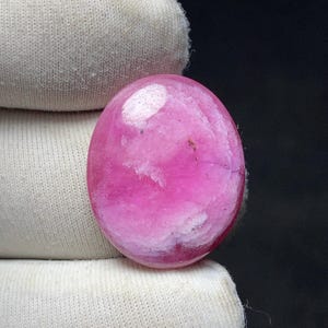 May include: A polished, oval-shaped gemstone in shades of pink and white. The stone has a smooth, glossy surface with a marbled appearance. The gemstone is likely a cabochon, suitable for jewelry making or collecting.