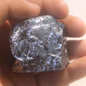 May include: A raw, jagged chunk of metallic silicon with a highly reflective, silver-grey surface. The mineral specimen features sharp, crystalline facets that catch the light, creating a brilliant, mirror-like sheen across its irregular, blocky structure.