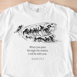 May include: White t-shirt with a black wave graphic and the text "When you pass through the waters, I will be with you. Isaiah 43:2." Also shown are blue jeans and blue canvas sneakers.