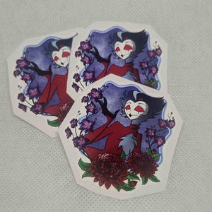 May include: Three hexagonal stickers featuring a stylised owl-like character with black and white feathers, red eyes, and a red garment. The character is surrounded by purple floral branches and dark red chrysanthemum flowers against a blue background.