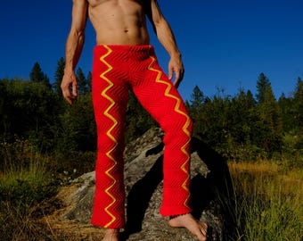 May include: Red knitted trousers featuring a yellow zigzag design. The trousers have a fitted style and are made from a textured fabric. The image shows the trousers outdoors against a backdrop of trees and a blue sky.