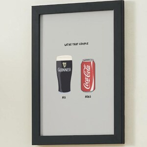 Puede incluir: Impresi&oacute;n enmarcada con fondo gris. Presenta un vaso de pinta Guinness etiquetado "HIS" y una lata de Coca-Cola etiquetada "HERS". El texto "WE'RE THAT COUPLE" est&aacute; encima de las im&aacute;genes. El marco es negro.