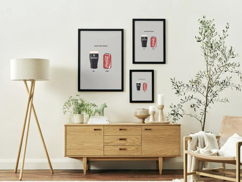 Puede incluir: Tres impresiones enmarcadas con marcos negros cuelgan de una pared blanca. Cada impresi&oacute;n presenta un vaso de Guinness y una lata de Coca-Cola. Las impresiones est&aacute;n sobre un mueble de madera. Una l&aacute;mpara de pie tambi&eacute;n es visible.