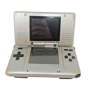 Może przedstawiać: Srebrna konsola do gier przenośna Nintendo DS, otwarta. Konsola posiada górny ekran, dolny ekran, pad kierunkowy i przyciski akcji. Logo Nintendo DS jest widoczne na dolnej połowie konsoli.