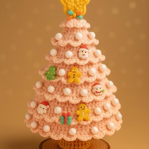 May include: A handmade, pink crocheted Christmas tree with white bead accents and festive embellishments. The tree is adorned with small Santa faces, gingerbread men, a green tree, and a wrapped gift. A yellow star tops the tree, which sits on a wooden base.