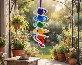 Peut inclure: Un mobile en crochet en forme de spirale suspendu, composé de six sphères disposées en dégradé arc-en-ciel : violet, bleu, vert, jaune, orange et rouge. Chaque sphère est entourée d'un anneau en crochet blanc, suspendu par un cordon violet.
