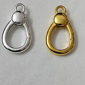 May include: Two teardrop-shaped spring gate rings, one in a polished silver-tone finish and one in a polished gold-tone finish. Each piece features a circular base with a hinged mechanism at the top, allowing the ring to open for attaching items.