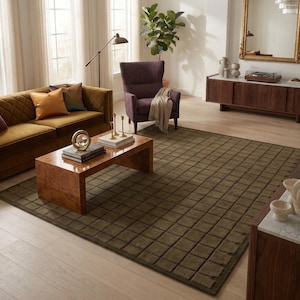 May include: A living room scene featuring a brown velvet sofa with colorful pillows, a patterned rug, and a wooden coffee table. A purple armchair and a large mirror add to the room's decor. The rug has a grid pattern.