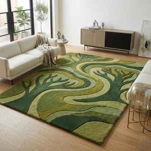 May include: A green area rug with a tree design. The rug features a pattern of stylized trees and flowing lines in shades of green and cream. The rug is rectangular and placed on a hardwood floor.