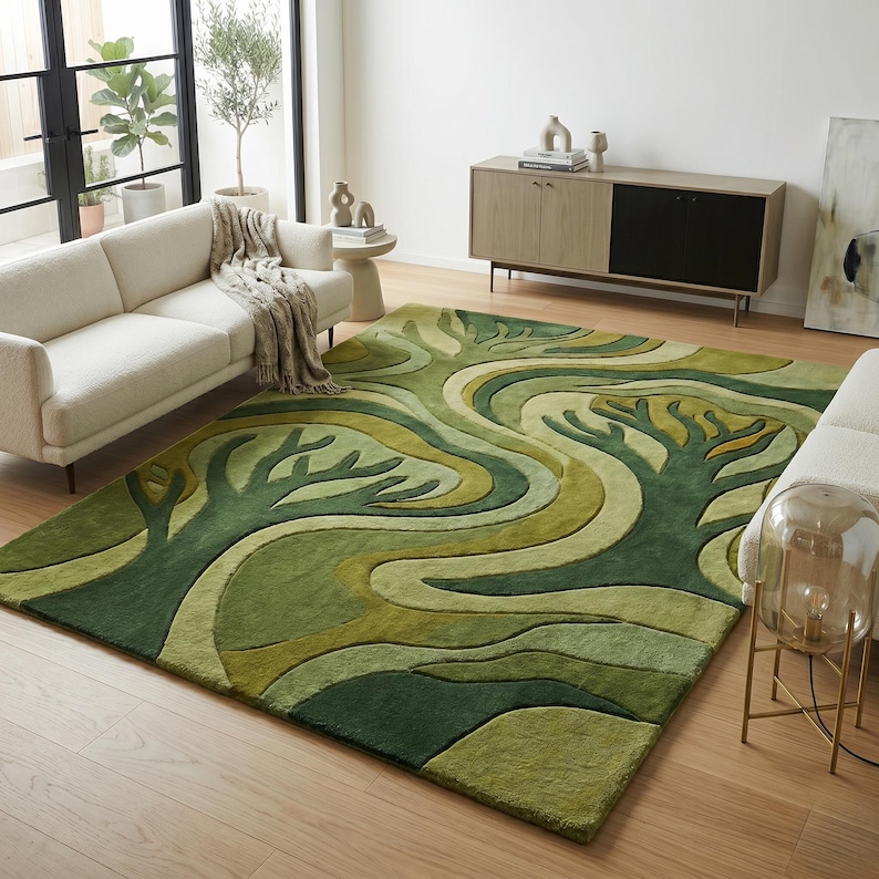 May include: A green area rug with a tree design. The rug features a pattern of stylized trees and flowing lines in shades of green and cream. The rug is rectangular and placed on a hardwood floor.