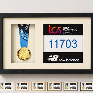Könnte beinhalten: Gerahmte Präsentation mit einer Goldmedaille an einem blauen Band und einer Startnummer mit der Nummer 11703. Der Rahmen enthält die Logos von TCS und New Balance, ideal für Lauferfolge.