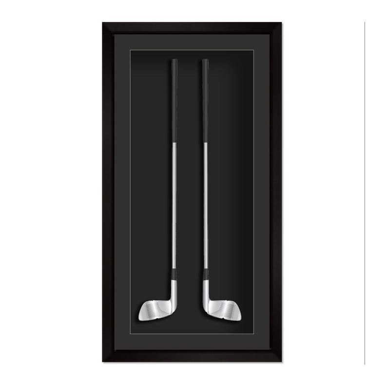 May include: Two golf clubs displayed in a black shadow box frame. The clubs have silver heads and shafts with black grips, set against a black background. The frame is rectangular and has a dark border.