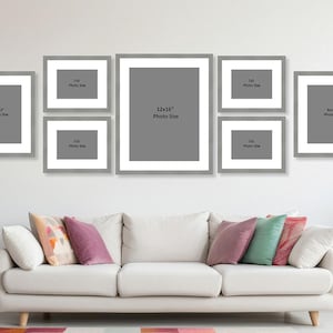 Può includere: Una composizione da parete per galleria con otto foto incorniciate grigie di varie dimensioni. La cornice più grande è 30x41 cm, e le altre sono 20x25 cm e 18x13 cm. Sotto, un divano bianco con cuscini colorati e un tavolino.